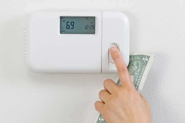 homeowner adjusting thermostat while holding money depicting Home Heating Oil Efficiency