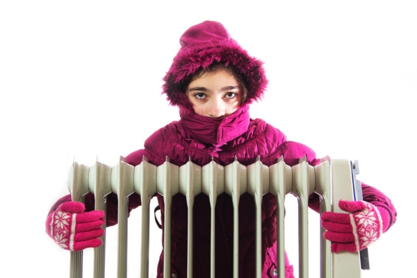 young girl wearing full winter outfit hugging space heater due to cold spots in the house