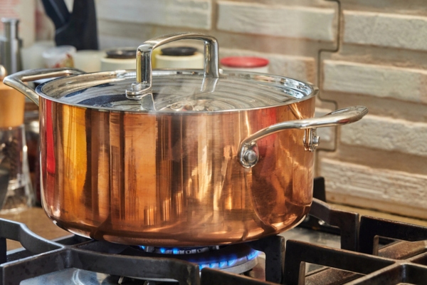 Copper saucepan with lid with dish is cooked over fire on a gas stove