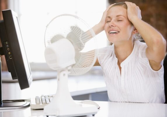 woman feeling cool in front of a desk fan due to heat pump blowing warm air in cool mode